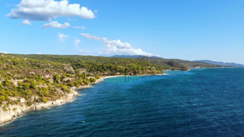 Video - Aerial drone view of the Aegean sea rocky coast with greenery along the shore, waves of the sea in Greece