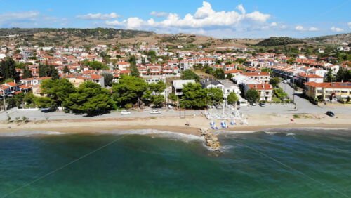 Video - Aerial drone view of the Aegean sea coast in Nikiti, Greece. Beach with terraces, umbrellas and sunbeds on embankment street, multiple buildings