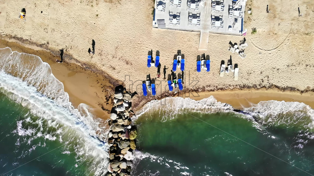 Video - Aerial drone view of the Aegean sea coast in Nikiti, Greece. Beach with waves of the sea, sunbeds with resting people and terrace top view