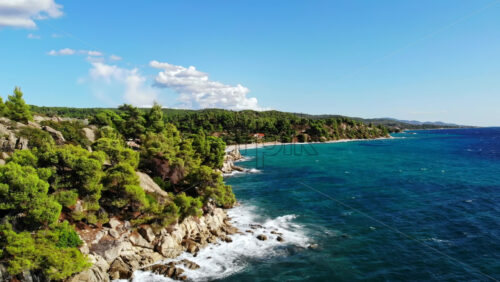 Video - Aerial drone view of the Aegean sea rocky coast with greenery and road along the shore, waves of the sea in Greece