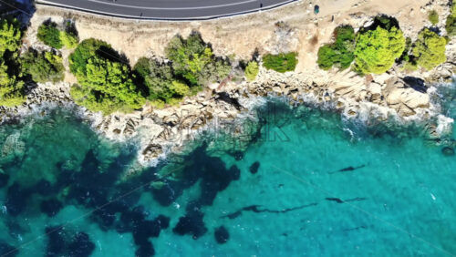 Video - Aerial drone view of the Aegean sea rocky coast with greenery and road along the shore, waves of the sea in Greece