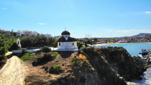 Video - Aerial drone view of the Nea Roda church situated on a hill, Greece. Aegean sea coast with town on the background