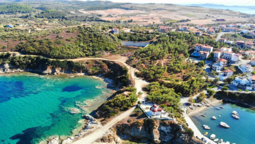 Video - Aerial drone view of the Nea Roda situated on the Aegean sea coast, Greece. Multiple buildings with greenery, church near the shore