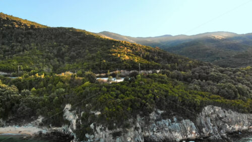 Video - Aerial drone view of the Aegean sea rocky coast with green hills neat the shore, observation point with a couple on the side of a road in Greece