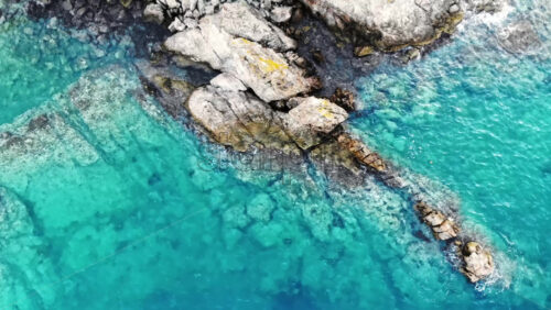 Video - Aerial drone view of the Aegean sea rocky coast with rocks in the blue transparent water, top view, Greece