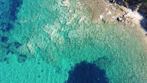 Video - Aerial drone view of the Aegean sea rocky coast with rocks in the blue transparent water, top view, Greece