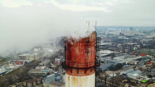 Video - Aerial drone view of thermal station with smoke coming out of the tube. Buildings, roads and bare trees on the background. Cloudy weather. Chisinau, Moldova