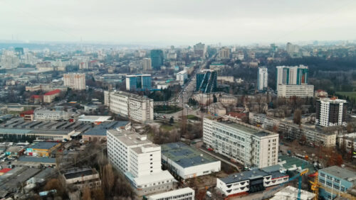 Video - Aerial drone view of Chisinau. Panorama view of multiple buildings, roads with moving cars and bare trees. Cloudy weather. Moldova