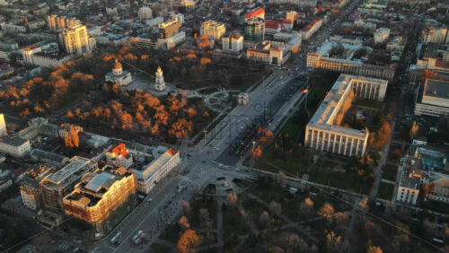 Video - Aerial drone view of Chisinau at sunset. Panorama view of multiple buildings in city center, roads with moving cars, central park with bare trees. Moldova