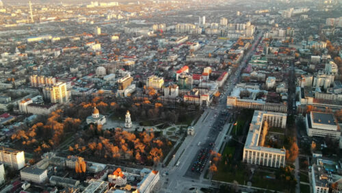Video - Aerial drone view of Chisinau at sunset. Panorama view of multiple buildings in city center, roads with moving cars, central park with bare trees. Moldova