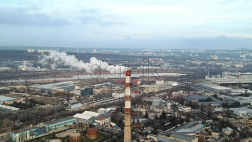 Video - Aerial drone view of thermal station with smoke coming out of the tube. Buildings, roads, lake and bare trees on the background. Cloudy weather. Chisinau, Moldova
