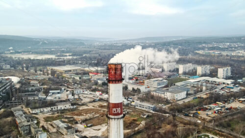 Video - Aerial drone view of thermal station with smoke coming out of the tube. Buildings, roads and bare trees on the background. Cloudy weather. Chisinau, Moldova