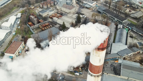 Video - Aerial drone view of thermal station with smoke coming out of the tube. Buildings, roads and bare trees on the background. Cloudy weather. Chisinau, Moldova