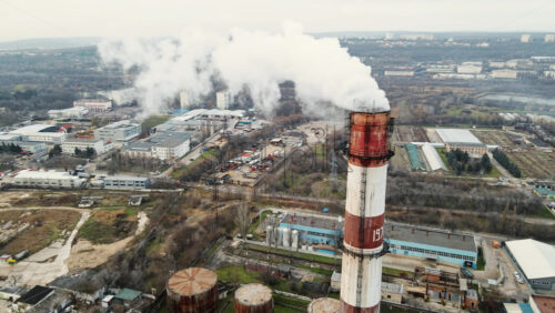 Video - Aerial drone view of thermal station with smoke coming out of the tube. Buildings, roads and bare trees on the background. Cloudy weather. Chisinau, Moldova