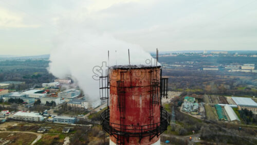 Video - Aerial drone view of thermal station with smoke coming out of the tube. Buildings, roads and bare trees on the background. Cloudy weather. Chisinau, Moldova