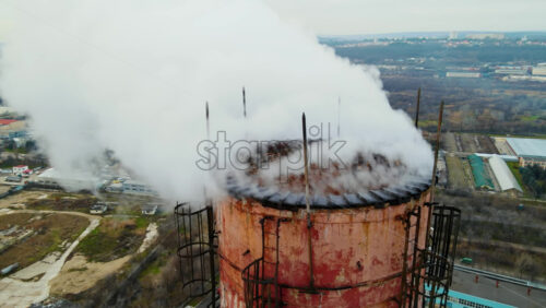 Video - Aerial drone view of thermal station with smoke coming out of the tube. Buildings, roads and bare trees on the background. Cloudy weather. Chisinau, Moldova