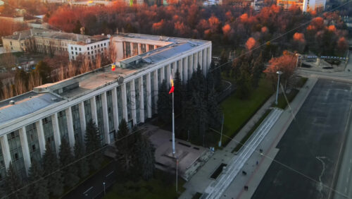 Video - Aerial drone view of Government House at sunset. Building with flag and road in front of it, bare trees in Chisinau, Moldova