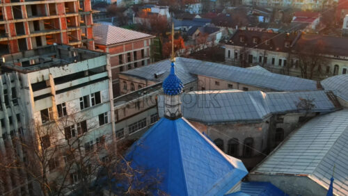Video - Aerial drone view of a church with blue roof, bare trees, old and unfinished buildings around it in Chisinau, Moldova