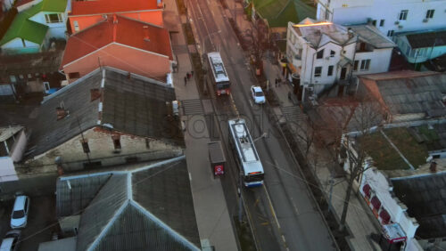 Video - CHISINAU, MOLDOVA - JANUARY 1, 2021: Aerial drone view of a street at sunset. View of buildings, road with moving buses, walking people, bare trees