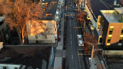 Video - CHISINAU, MOLDOVA - JANUARY 1, 2021: Aerial drone view of a street at sunset. View of buildings, road with moving buses and cars, walking people, bare trees