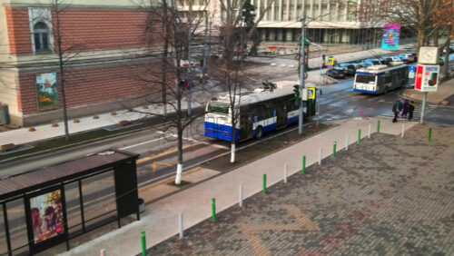 Video - CHISINAU, MOLDOVA - JANUARY 1, 2021: Aerial drone view of a bus stop with moving buses and parked cars, walking people, bare trees, square