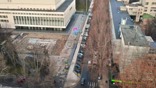 Video - CHISINAU, MOLDOVA - JANUARY 1, 2021: Aerial drone view of a street, road with moving and parked cars, walking people, bare trees and a square