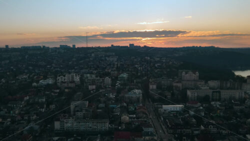 Video - Aerial drone view of Chisinau at sunset. Panorama view of multiple buildings, roads with moving cars, bare trees, park, lake and hills. Moldova