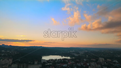 Video - Aerial drone view of Chisinau at sunset. Panorama view of multiple buildings, bare trees, park, lake and hills. Moldova
