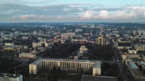 Video - Aerial drone view of Chisinau at sunset. Panorama view of the city center with the Government House and central park, multiple buildings, roads with moving cars, bare trees. Moldova