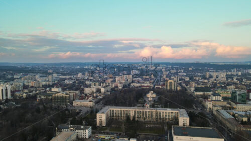 Video - Aerial drone view of Chisinau at sunset. Panorama view of the city center with the Government House and central park, multiple buildings, roads with moving cars, bare trees. Moldova