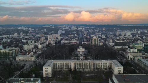 Video - Aerial drone view of Chisinau at sunset. Panorama view of the city center with the Government House and central park, multiple buildings, roads with moving cars, bare trees. Moldova