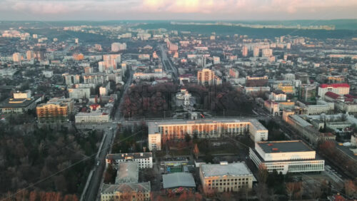 Video - Aerial drone view of Chisinau at sunset. Panorama view of the city center with the Government House and two central parks, multiple buildings, roads with moving cars, bare trees. Moldova