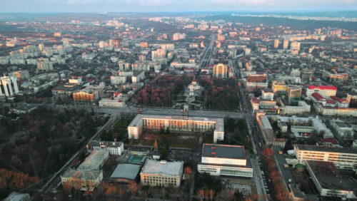 Video - Aerial drone view of Chisinau at sunset. Panorama view of the city center with the Government House and two central parks, multiple buildings, roads with moving cars, bare trees. Moldova
