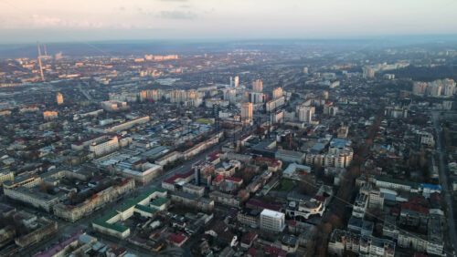 Video - Aerial drone view of Chisinau at sunset. Panorama view of multiple buildings, roads with moving cars, bare trees, park, lake and hills. Moldova