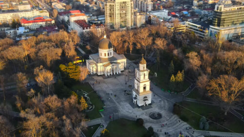 Video - Aerial drone view of Chisinau downtown. Panorama view of central park with bare trees and walking people, catheral, buildings on the background. Moldova