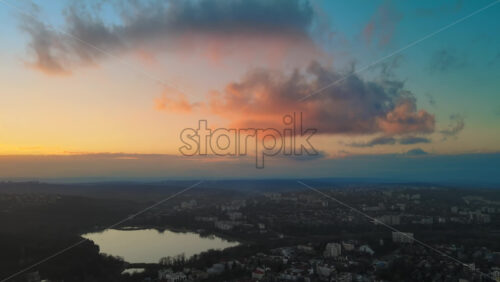 Video - Aerial drone view of Chisinau at sunset. Panorama view of multiple buildings, bare trees, park, lake and hills. Moldova