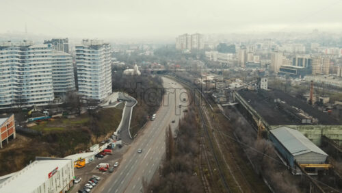 Video - CHISINAU, MOLDOVA - JANUARY 1, 2021: Aerial drone panorama view of a road view of a road with moving cars, residential buildings, railway and bare trees