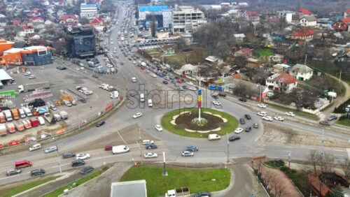 Video - CHISINAU, MOLDOVA - JANUARY 1, 2021: Aerial drone view of a road with roundabout intersection and multiple moving cars, residential buildings, wholesale store and bare trees
