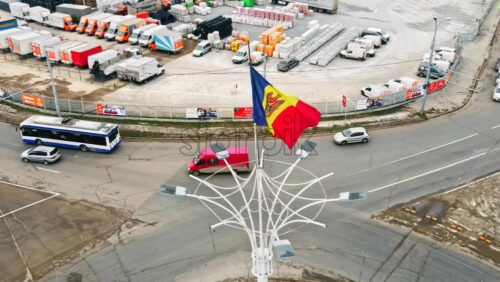 Video - CHISINAU, MOLDOVA - JANUARY 1, 2021: Aerial drone view of the Moldavian flag located on the roundabout intersection and multiple moving cars, residential buildings, wholesale store on the background