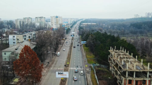 Video - CHISINAU, MOLDOVA - JANUARY 1, 2021: Aerial drone panorama view of a road with moving cars, residential buildings, park and bare trees