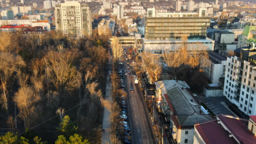 Video - CHISINAU, MOLDOVA - JANUARY 1, 2021: Aerial drone view of a street with multiple buildings, road with moving cars and bare trees. Moldova
