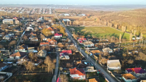 Video - Aerial drone view of a village. View of multiple residential buildings, country roads, bare trees and football field. Sunny weather. Moldova