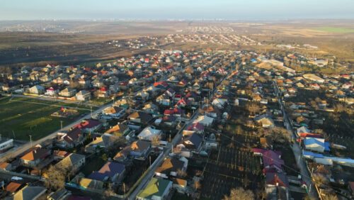 Video - Aerial drone view of a village. View of multiple residential buildings, country roads, bare trees and football field. City on the background. Sunny weather. Moldova