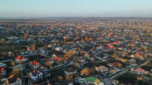 Video - Aerial drone view of a village. View of multiple residential buildings, country roads, bare trees. City on the background. Sunny weather. Moldova