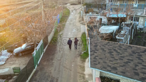Video - View of a two walking men on a country road and talking in a village. Residential buildings and bare trees. Moldova