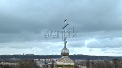 Video - Aerial drone view of a metal cross on a church in Chisinau, Moldova. Cityscape on the background, Cloudy weather, bare trees, winter