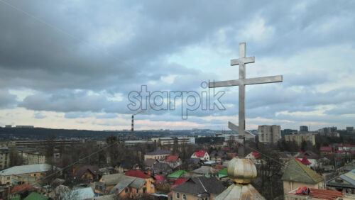 Video - Aerial drone view of a metal cross on a church in Chisinau, Moldova. Cityscape on the background, Cloudy weather, bare trees, winter