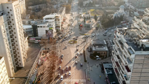 Video - CHISINAU, MOLDOVA - JANUARY 15, 2021: Aerial drone view of city at sunset. Multiple residential buildings, stores, road with roundabout and moving cars. Bare trees, winter