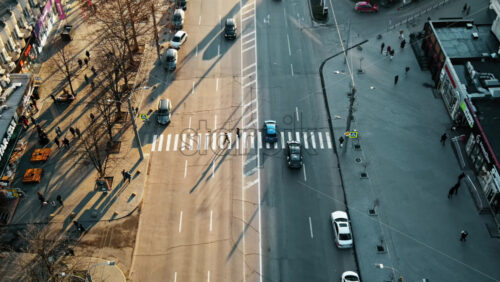 Video - CHISINAU, MOLDOVA - JANUARY 15, 2021: Aerial drone view of street at sunset. Multiple walking people crossing the road, stores, road. Bare trees, winter