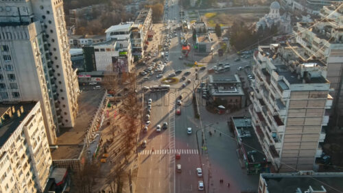 Video - CHISINAU, MOLDOVA - JANUARY 15, 2021: Aerial drone view of city at sunset. Multiple residential buildings, stores, road with roundabout and moving cars. Bare trees, winter